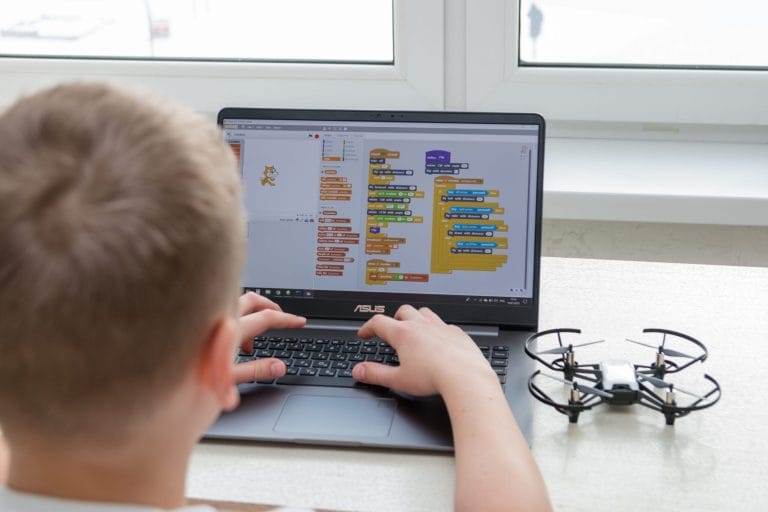 A young student programs a Tello drone using Scratch block coding on a laptop in our drone course for kids